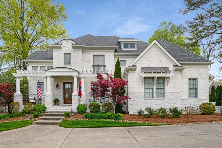 White brick home with a covered entry, front garden and mature trees.