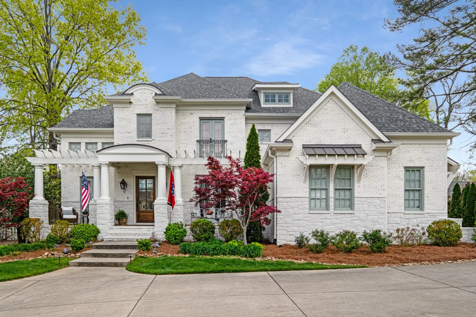 White brick home with a covered entry, front garden and mature trees.