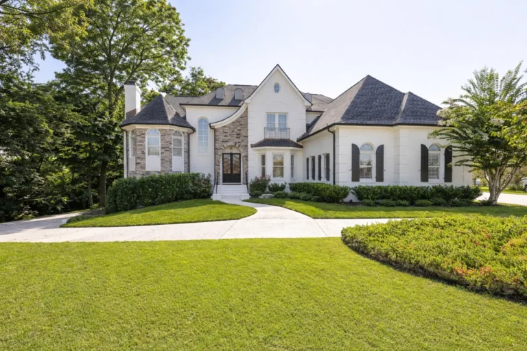 White and stone home with arched windows, a curved walkway and mature landscaping.