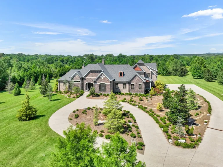 Elevated view of a large brick home with a circular driveway and broad lawn.