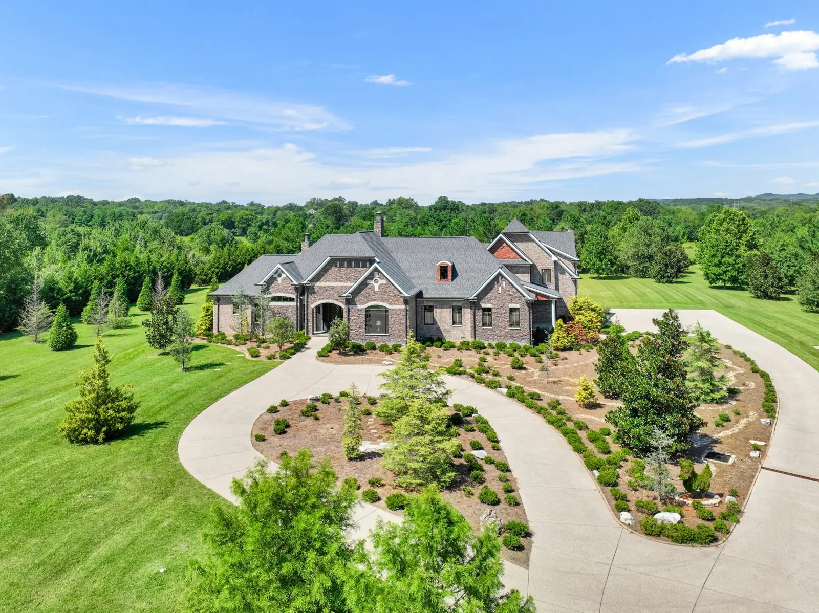 Elevated view of a large brick home with a circular driveway and broad lawn.