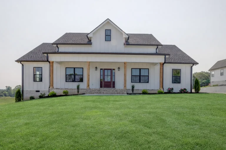 White farmhouse-style home with wood porch posts and a broad front lawn.