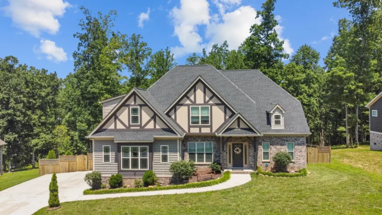 Gabled home with decorative timber trim, brick and gray siding beside mature woods.