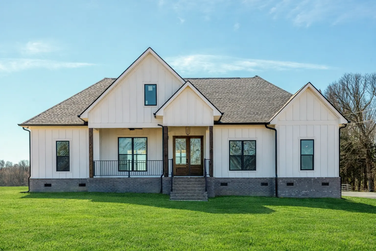 White home with a raised covered porch, black railings and double wood front doors.