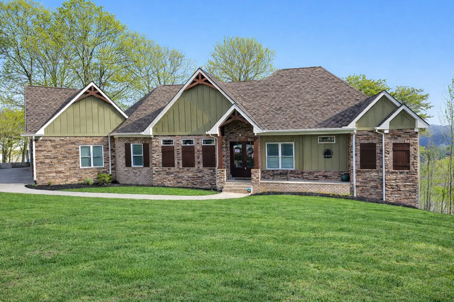 Stone-front home with green siding, a covered entry and a broad front lawn.