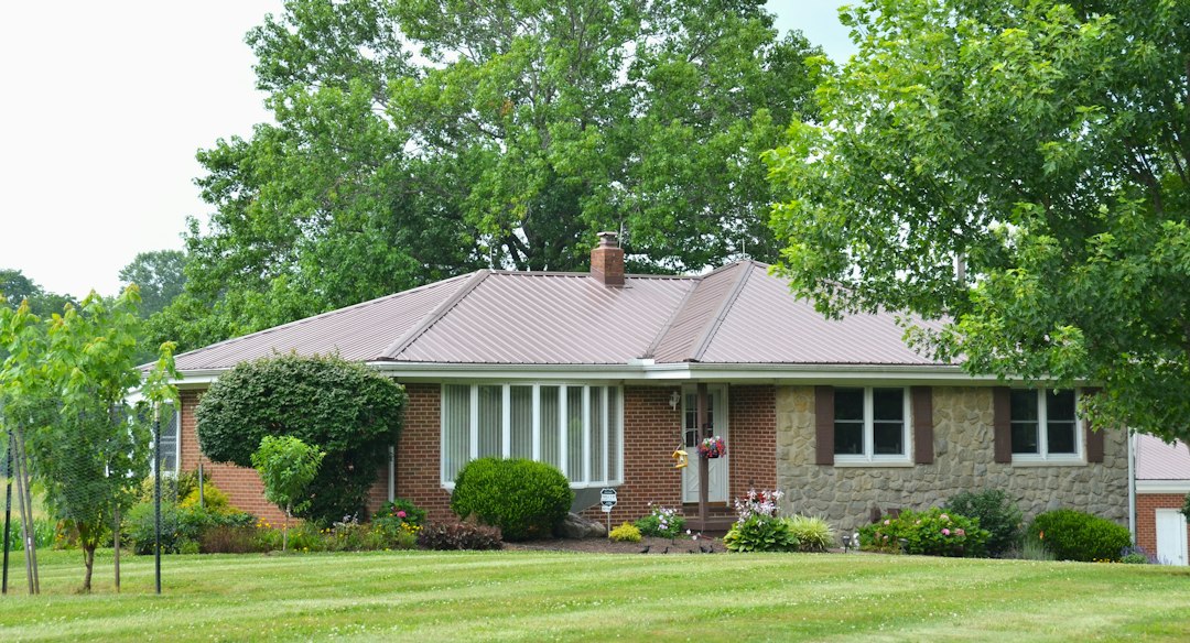 Brick ranch house with a metal roof and mature trees; illustrative stock photograph